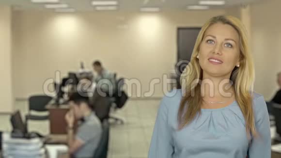 可爱的金发女人在电话里讲话的特写镜头她微笑着站在一边蓝色固体背景现代办公室视频的预览图