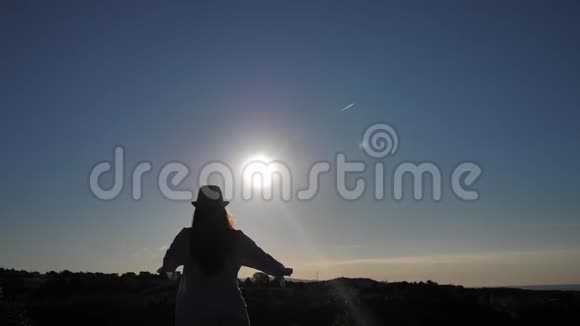 女人站在上面看着城市和大海在日落时举起双手向太阳看视频的预览图