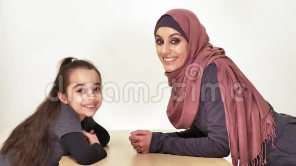 年轻漂亮的妈妈和她的小女儿戴着头巾看着镜头笑着说家庭幸福的家庭观念视频的预览图