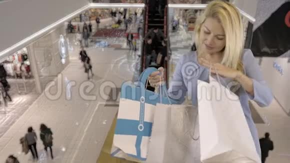 美丽的白种人金发碧眼的女性穿着蓝色的裙子站在购物中心的时候正在寻找购物袋视频的预览图
