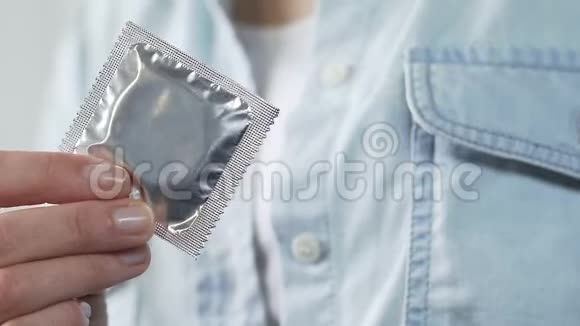 女孩的手拿着密封的避孕套把它放进衬衫口袋里避孕视频的预览图