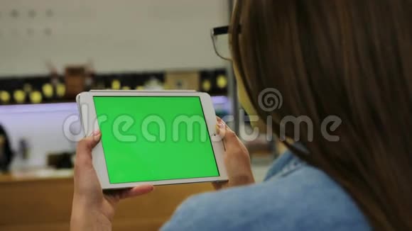 年轻有魅力的女人戴着眼镜在咖啡馆里用绿色屏幕在平板电脑上观看视频特写镜头铬键视频的预览图