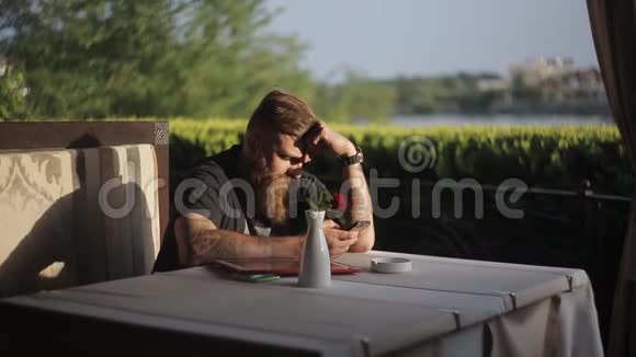 男人坐在自助餐厅或餐厅拿着智能手机看着它的屏幕使用小玩意的人视频的预览图