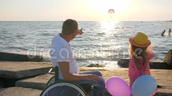 父亲坐轮椅孩子在海边孩子手里拿着多色气球视频的预览图