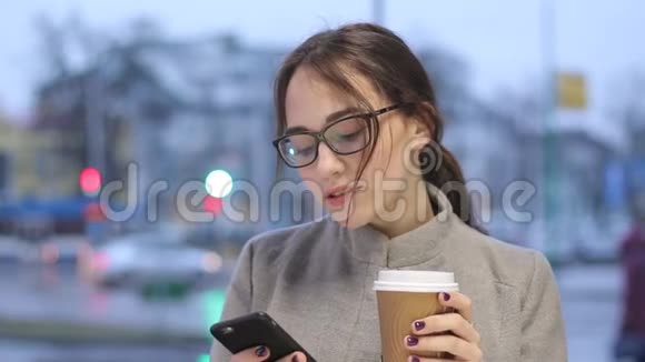 年轻的女性在户外喝咖啡在智能手机里浏览视频的预览图