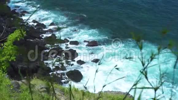 在绿色植物的背景下海浪拍打到岩石海滩汹涌的海浪溅到石崖泡沫和视频的预览图