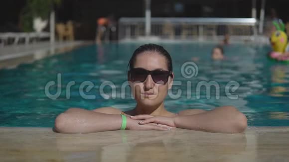 美丽的年轻女孩戴着太阳镜在室外游泳池游泳在阳光明媚的夏日视频的预览图