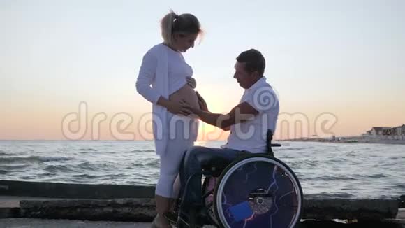 残疾人和妻子在晚上跳舞残疾配偶在轮椅上孕妇在日落时跳舞视频的预览图