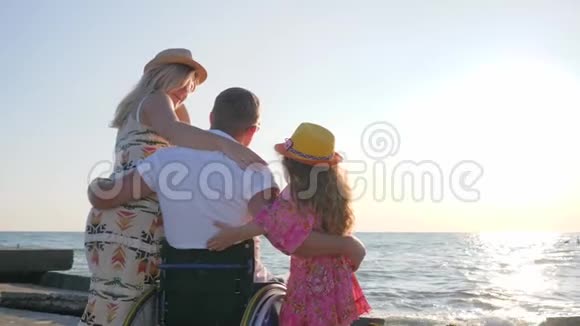 丈夫坐轮椅抱着妻子大肚子特写家人看着海浪残疾人抱着妻子和女儿视频的预览图