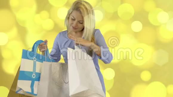 一位身穿蓝色连衣裙的白种人金发美女站在金色背景上正穿着购物袋视频的预览图