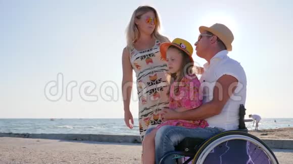幸福的家庭在蓝蓝的天空和大海的海岸上交流残疾的有怀孕的妻子和女儿拥抱视频的预览图