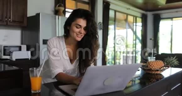 女孩使用笔记本电脑在厨房聊天在线年轻女子喝果汁工作室现代住宅视频的预览图