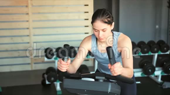 健身房里漂亮的女人用自行车锻炼腿部做有氧训练视频的预览图