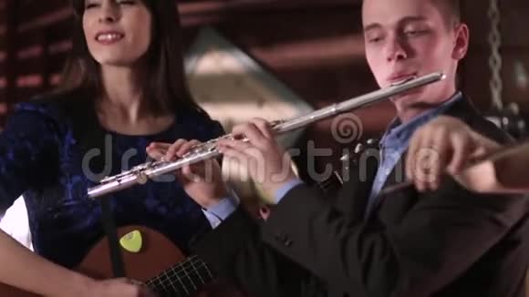 两个人音乐家复制音乐一个穿着夹克和衬衫的男人吹笛子一个穿着蓝色裙子的漂亮黑发女人吹笛子视频的预览图