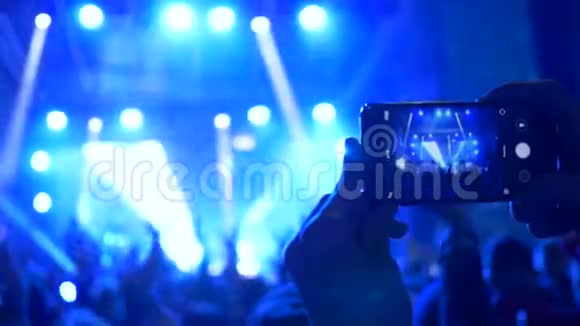 摇滚音乐会观众在手机上拍摄在明亮的灯光下表演音乐团体视频的预览图