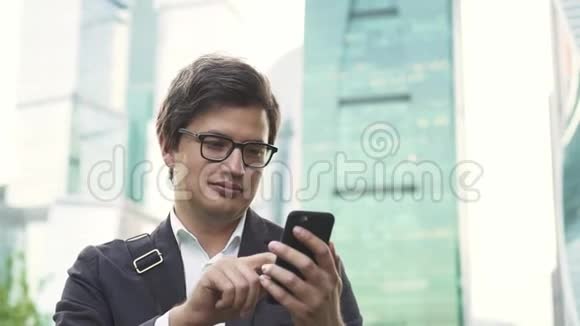 戴眼镜的英俊商人穿过莫斯科市的智能手机屏幕视频的预览图