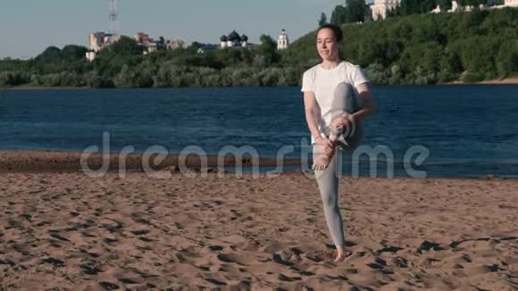 女人在城市河边的海滩上伸展瑜伽美丽的城市景色维里克哈萨纳姿势视频的预览图