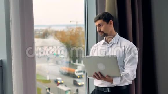 白天一个商人在一台银色笔记本电脑上工作站在一扇敞开的窗户附近视频的预览图