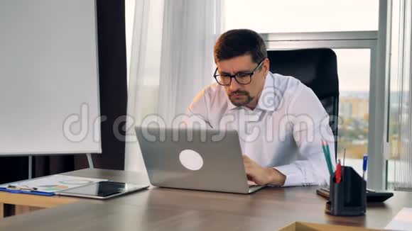 一个商人坐在他的办公桌前在笔记本电脑上打字视频的预览图