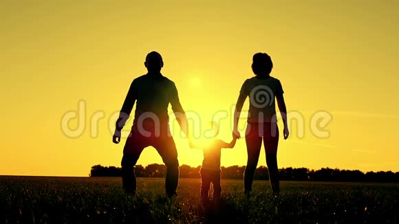 母亲和父亲牵着婴儿的手在日落时举起它的剪影幸福家庭的概念视频的预览图