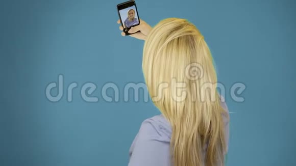 漂亮的女人在蓝色背景上用手机自拍微笑和旋转享受生活方式的概念视频的预览图