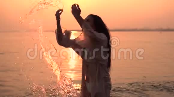 美丽的女孩做一个喷雾的手站在水中的背景下太阳有一个好心情慢慢慢慢视频的预览图