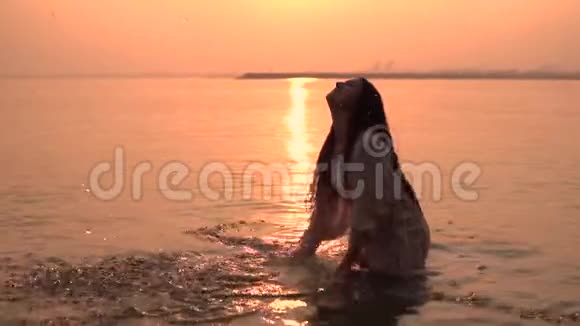 美丽的女孩做一个喷雾的手站在水中的背景下太阳有一个好心情慢慢慢慢视频的预览图