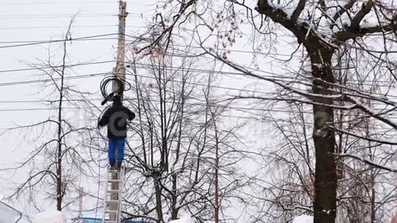 冬季城市电力线路的人修站在梯子上手里拿着电线后视图视频的预览图