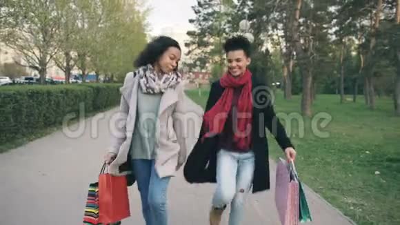 多利拍摄了两个迷人的混合种族妇女跳舞并玩得开心而步行下公园与购物袋快乐视频的预览图