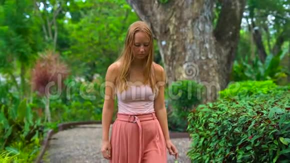 一名年轻女子在热带公园的反射路径上慢镜头视频的预览图