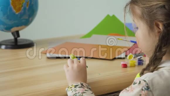 梳着辫子的小女孩坐在桌边画泥塑工艺品视频的预览图