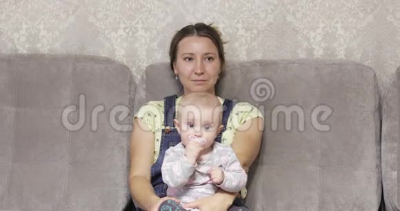 一位快乐的母亲坐在沙发上抱着一个孩子小女孩在玩奶嘴视频的预览图