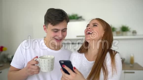 快乐的一对夫妻在家厨房吃早餐一起用智能手机上网尽情喝酒视频的预览图