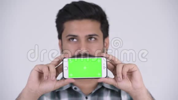 年轻的留胡子的印度男人一边看手机一边思考视频的预览图