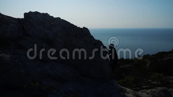 年轻的长发男子举起双手站在海面上一座山的顶端与美丽的山对着视频的预览图