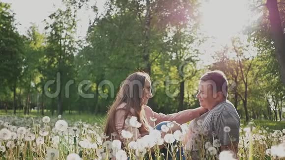 一对浪漫的夫妇在一片绿色的草地上在阳光下的许多蒲公英中他们互相看着对方眼睛视频的预览图