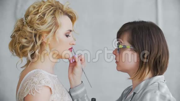化妆师用红色口红特写画一个金发女孩视频的预览图
