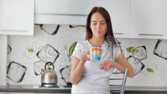 微笑的年轻女子端着一杯茶在厨房摆姿势视频的预览图