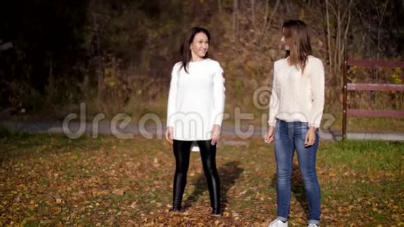 两个美丽的女人在秋天的花园里扔金叶女孩跳玩得开心像孩子一样4k60fps慢动作视频的预览图
