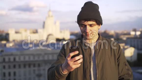 一个穿着便帽在屋顶发短信的年轻人视频的预览图