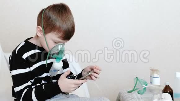 使用雾化器和吸入器进行治疗男孩通过吸入面罩吸入并在手机中玩游戏视频的预览图