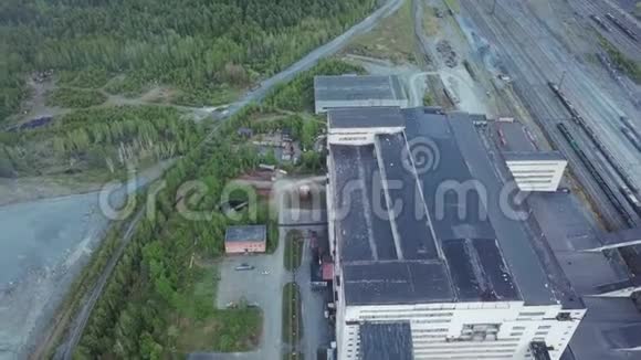 在铁路和废弃地面附近被森林包围的巨大灰色工业建筑的鸟瞰图工业区视频的预览图