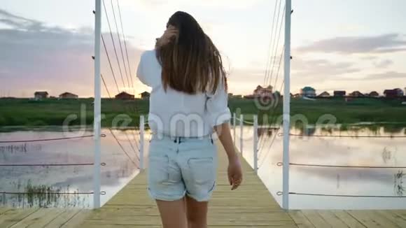 年轻女孩走在木桥上日落时走在湖边跟着投篮慢动作视频的预览图