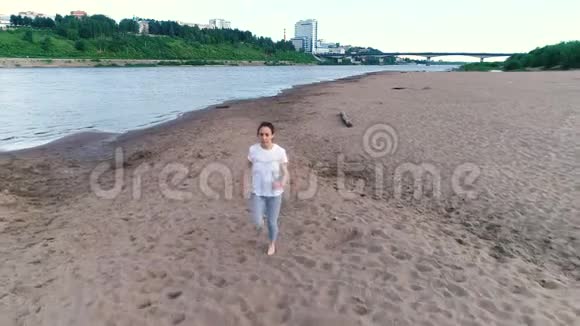 日落时分女人沿着河边的沙滩慢跑美丽的城市景色视频的预览图