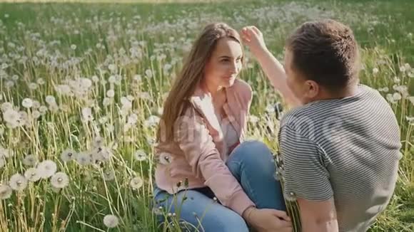 一对浪漫的夫妇在一片绿色的草地上在许多蒲公英中他们互相看着对方眼睛一起快乐夏季视频的预览图