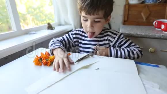 聪明的5岁男孩用剪刀热情地剪纸伸出舌头视频的预览图