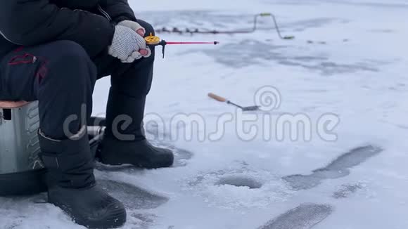 渔人手在冻江上的冻鱼竿上打鱼洞视频的预览图