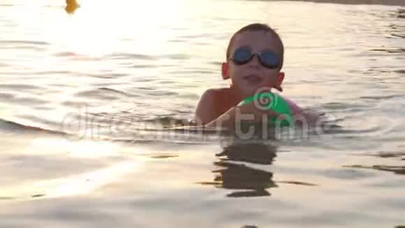 日落时分带球在海里游泳的男孩视频的预览图
