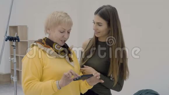 年轻和年老的女人在看智能手机屏幕时讨论制作的照片视频的预览图