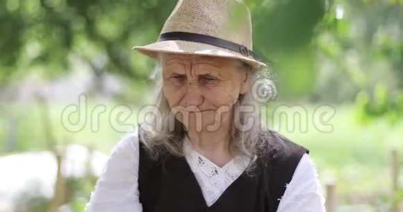 一个头发花白戴着草帽的快乐奶奶看着镜头吃东西视频的预览图
